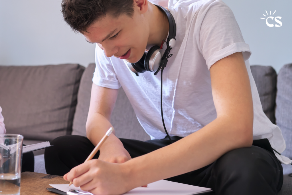 Teen writing in a journal with the CS logo