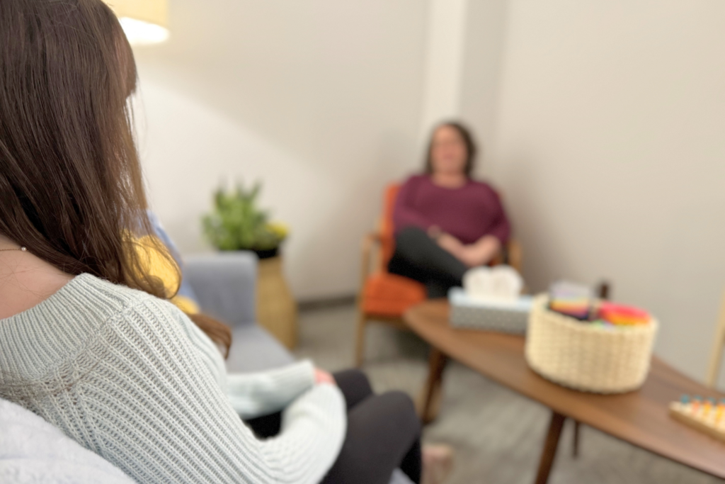Over the shoulder of a child in an office with a therapist in the background. 