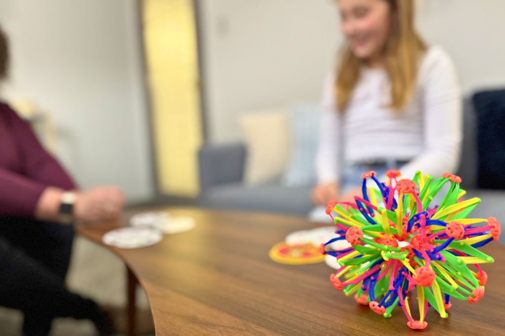 A kid smiling playing cards with a therapist, a concentration fidget in the foreground. 
