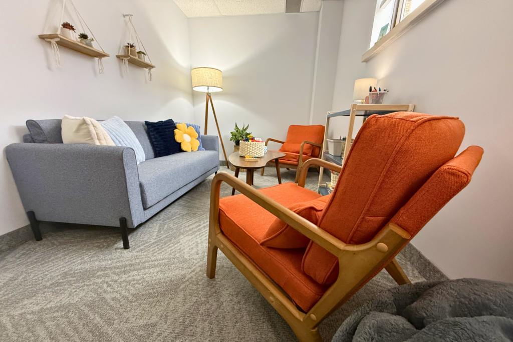 Therapist office space, warm light, bright orange chairs and a blue couch. 